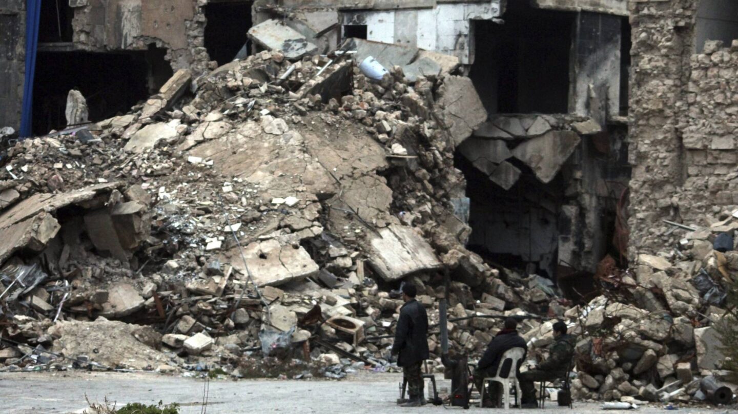 Un grupo de personas contemplan un edificio de Alepo en ruinas.
