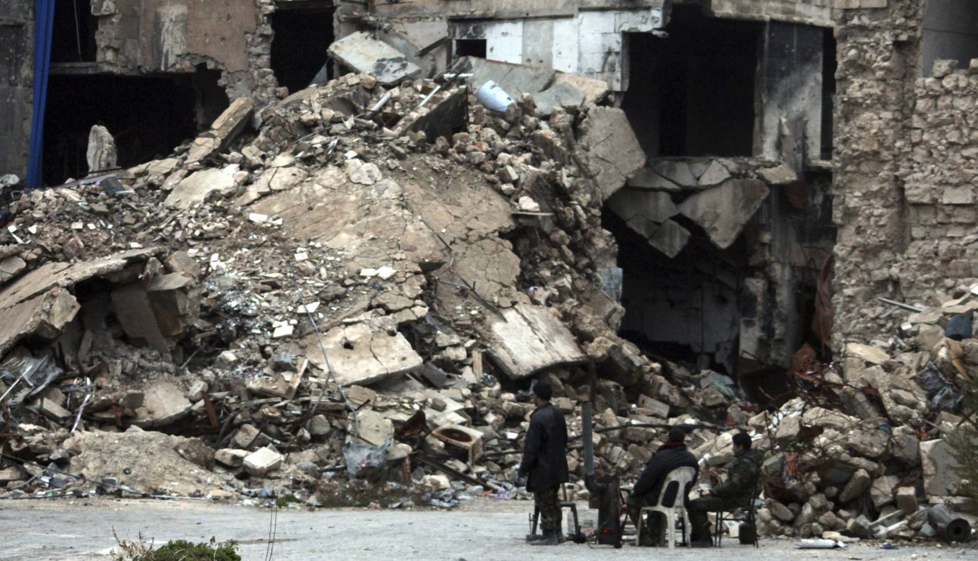 Un grupo de personas contemplan un edificio de Alepo en ruinas.