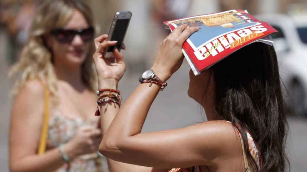 Una turista consulta su teléfono mientras se protege del sol en Sevilla.