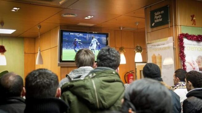 Un grupo de gente ve un partido de fútbol en la televisión de un bar.