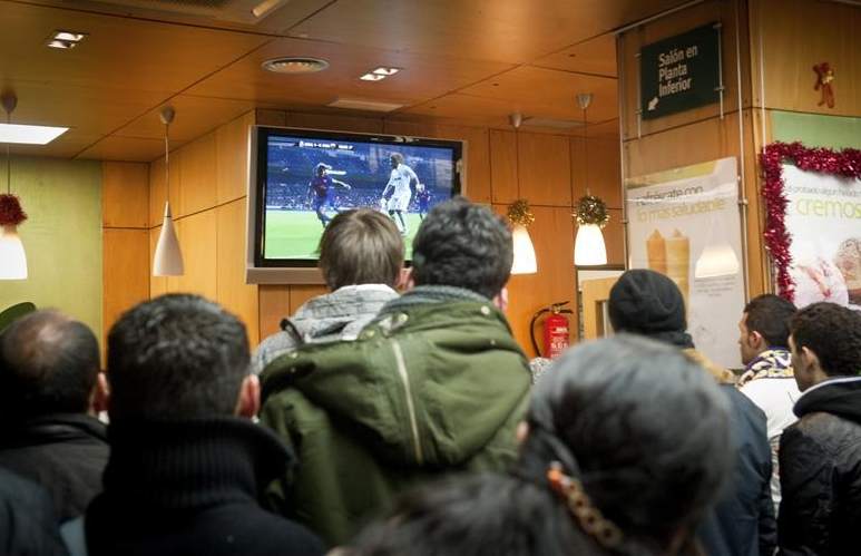 Un grupo de gente ve un partido de fútbol en la televisión de un bar.