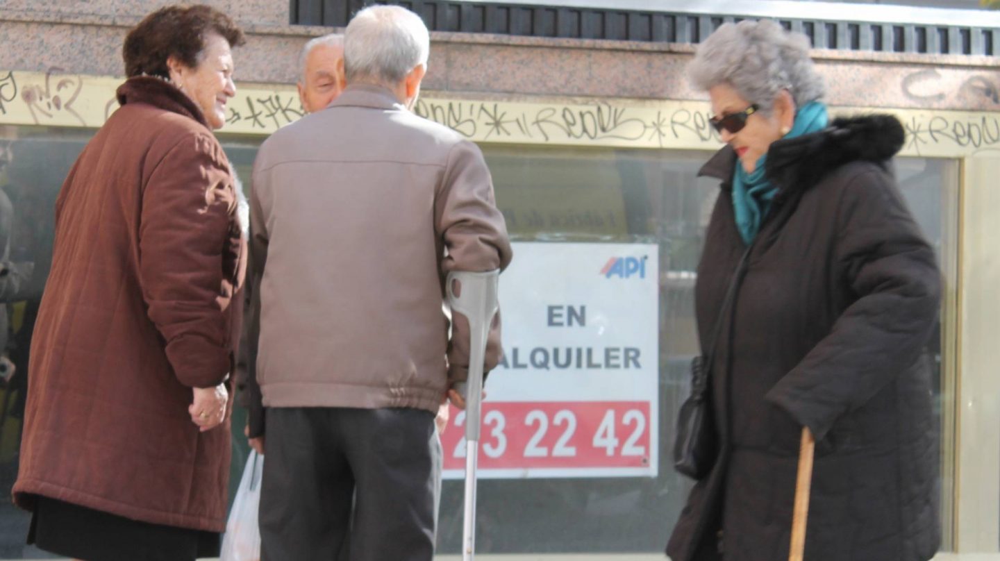 Grupo de personas mayores ante de un cartel de oferta inmobiliaria.