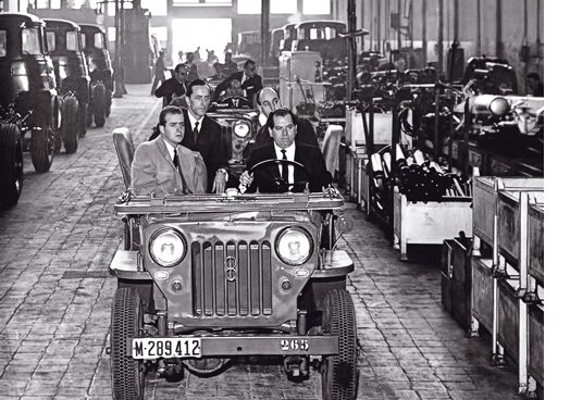 Eduardo Barreiros conduce un coche en su factoría junto al príncipe Juan Carlos.