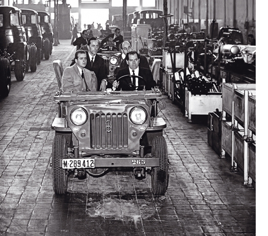 Eduardo Barreiros conduce un coche en su factoría junto al príncipe Juan Carlos.