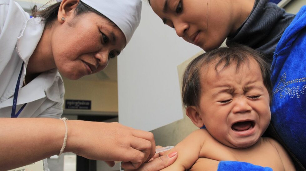 Una enfermera vacuna a un bebé sujetado por su madre en Camboya.