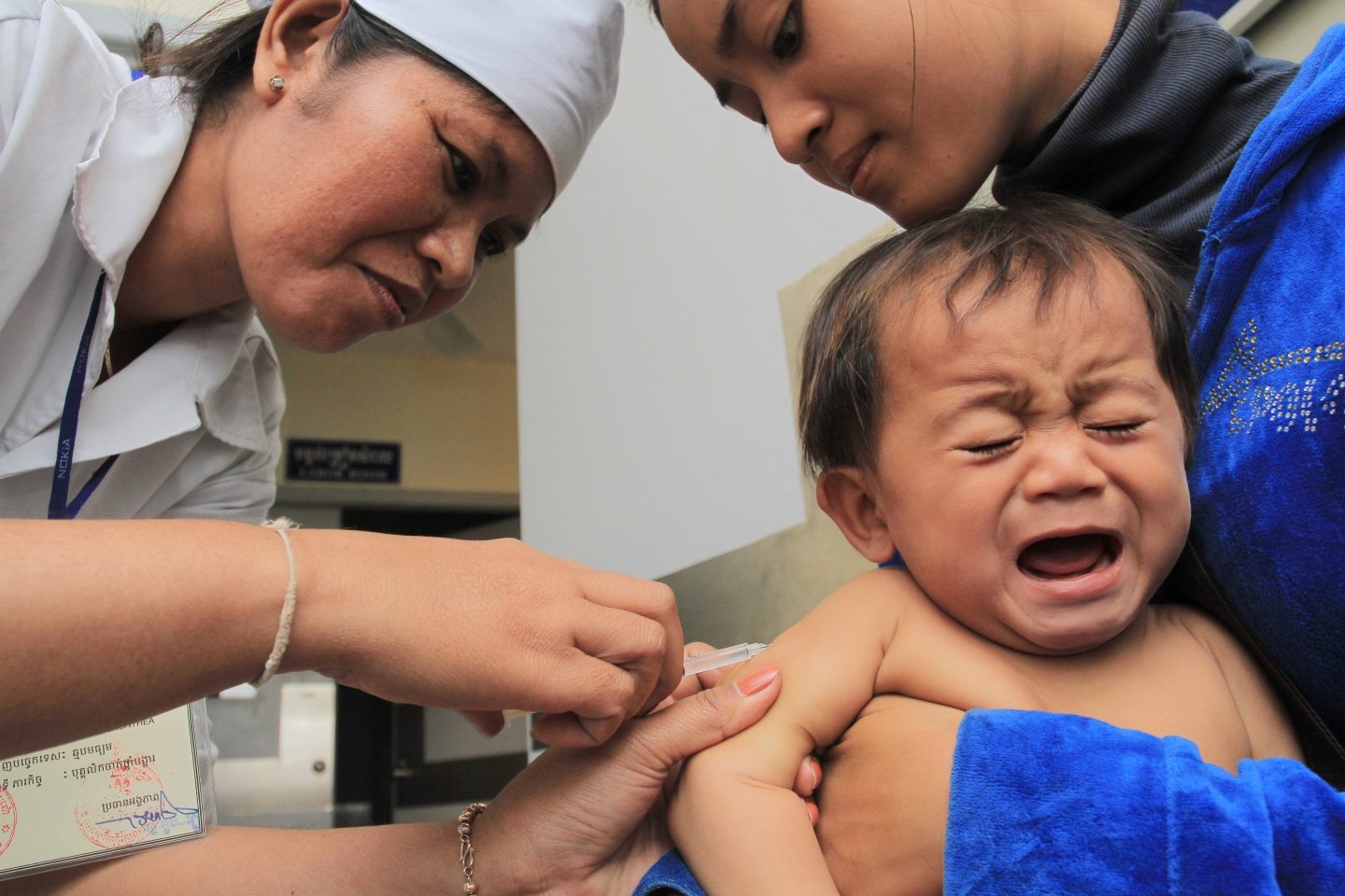 Una enfermera vacuna a un bebé sujetado por su madre en Camboya.