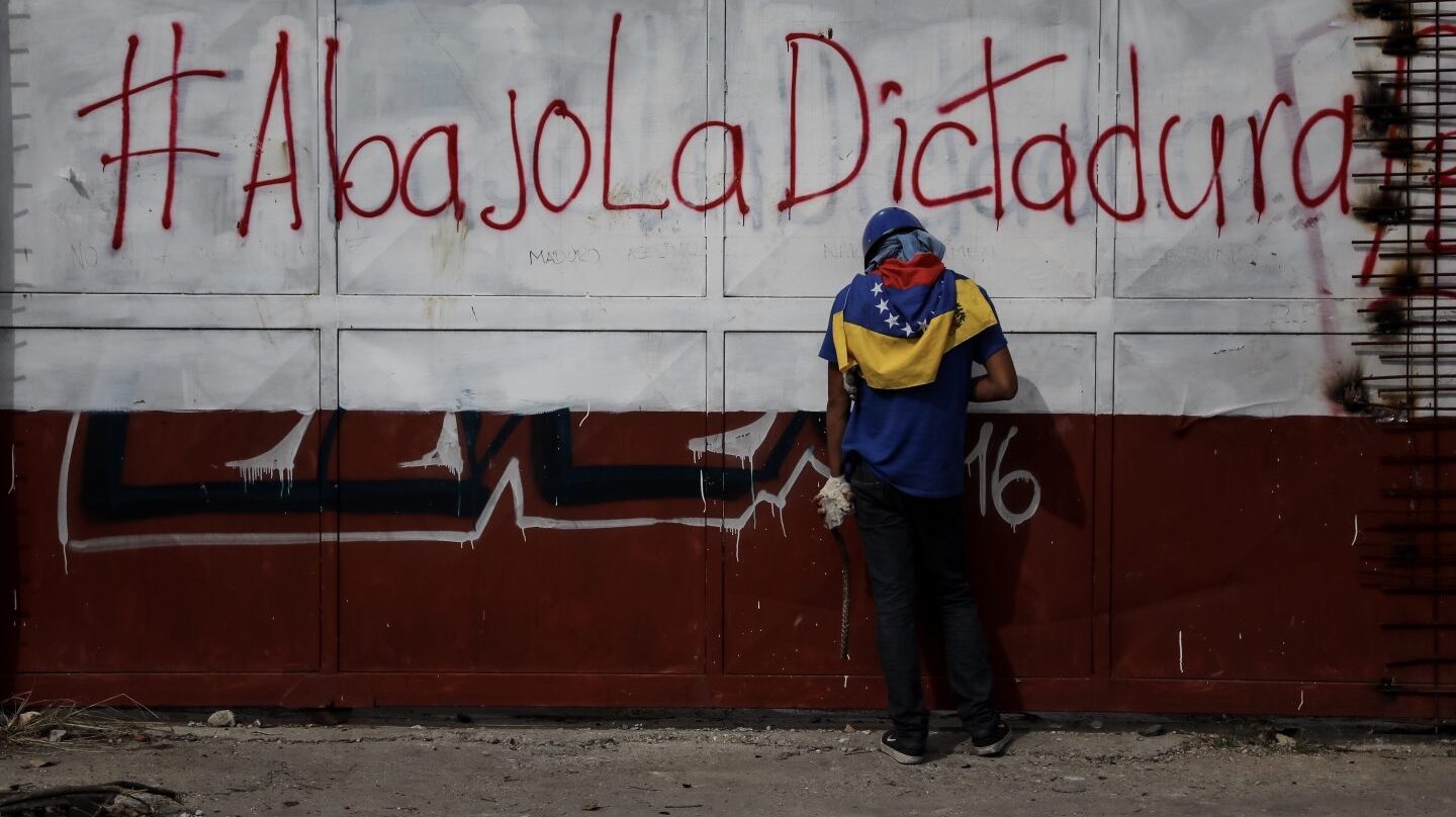 Un opositor hace un descanso junto a un cartel contrario al gobierno de Maduro.