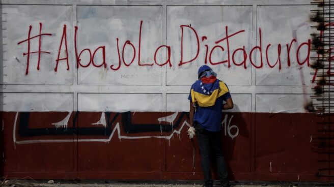 Un opositor hace un descanso junto a un cartel contrario al gobierno de Maduro.