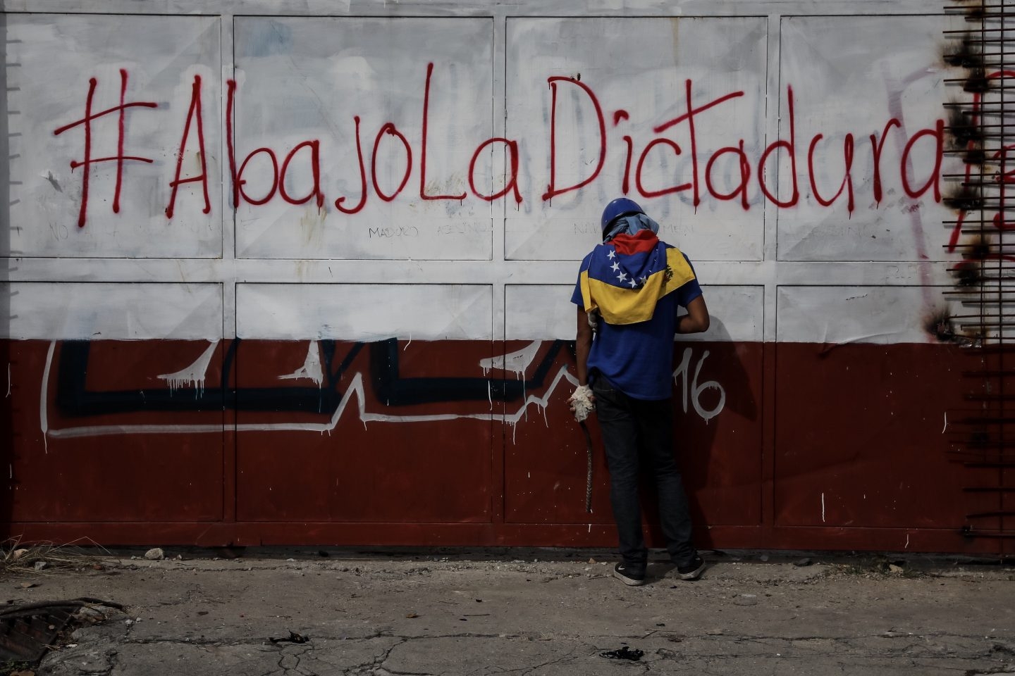 Un opositor hace un descanso junto a un cartel contrario al gobierno de Maduro.