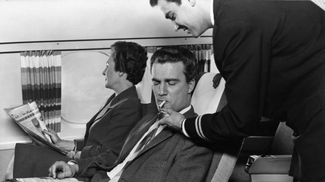 Personal de vuelo de KLM enciende un cigarrillo a un viajero, cuando la aerolínea permitía fumar.