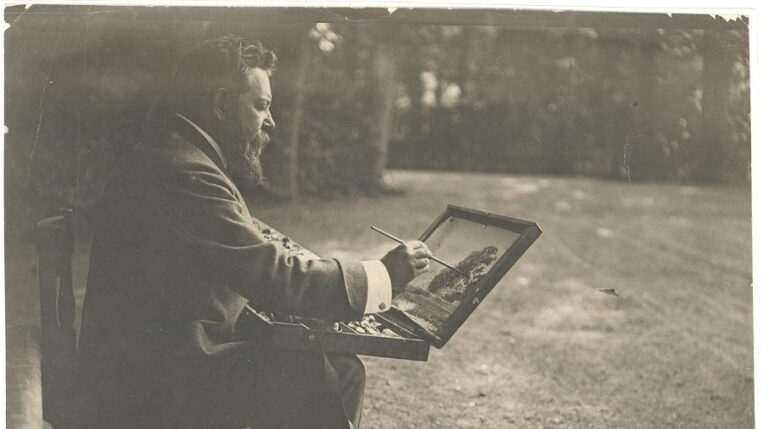 El pintor toma un apunte sentado, usando como caballete la tapa de su caja de pinturas, en los jardines de La Granja.