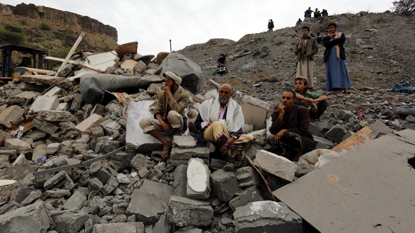 Varios yemeníes sentados entre los restos de un edificio tras un bombardeo de la coalición liderada por Arabia Saudí, en Saná.