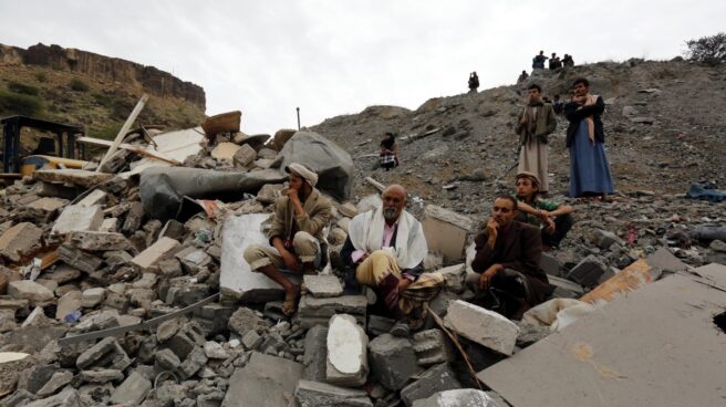 Varios yemeníes sentados entre los restos de un edificio tras un bombardeo de la coalición liderada por Arabia Saudí, en Saná.