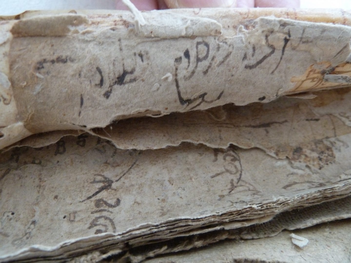 Detalle de varias capas de papel que forman el cartón oculto tras las cubiertas de piel que encuaderna el libro de cuentas manuscrito y que contienen escritura hebrea y latina (siglo XV)