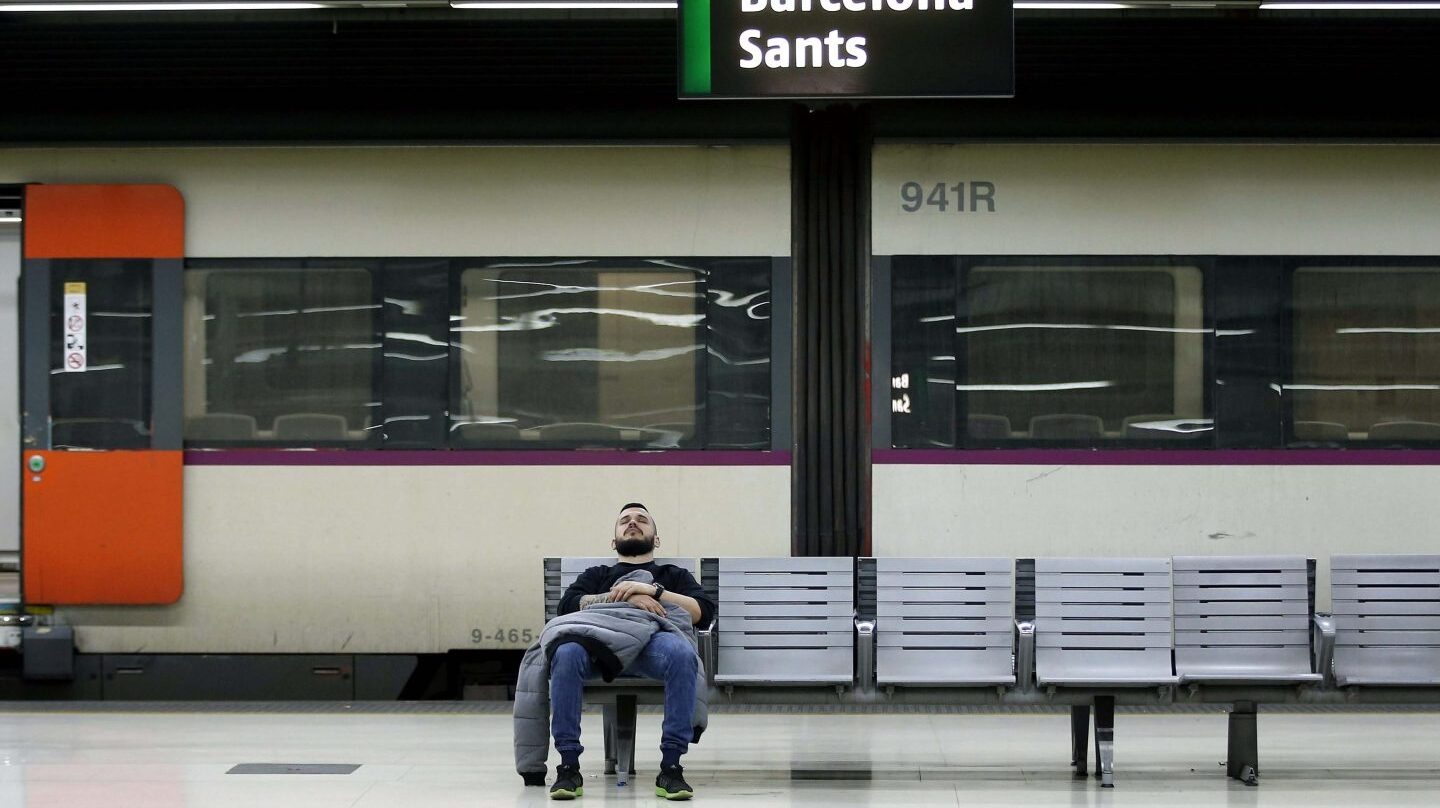 Un hombre descansa en un banco en el interior de la estación de Barcelona Sants.