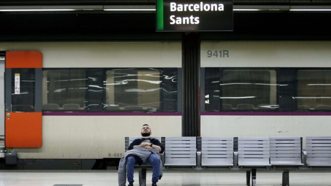 Un hombre descansa en un banco en el interior de la estación de Barcelona Sants.