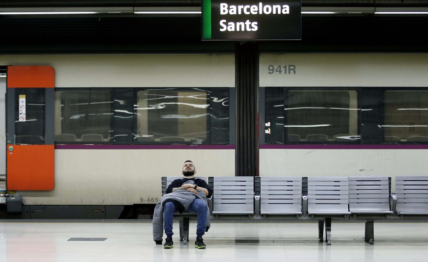 Un hombre descansa en un banco en el interior de la estación de Barcelona Sants.