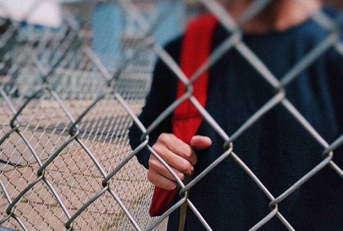 Un niño tras la valla de un patio de colegio.