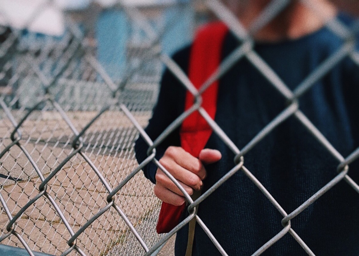 Un niño tras la valla de un patio de colegio.