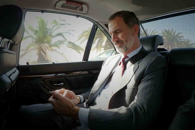 El Rey Felipe consulta el móvil en el coche oficial.