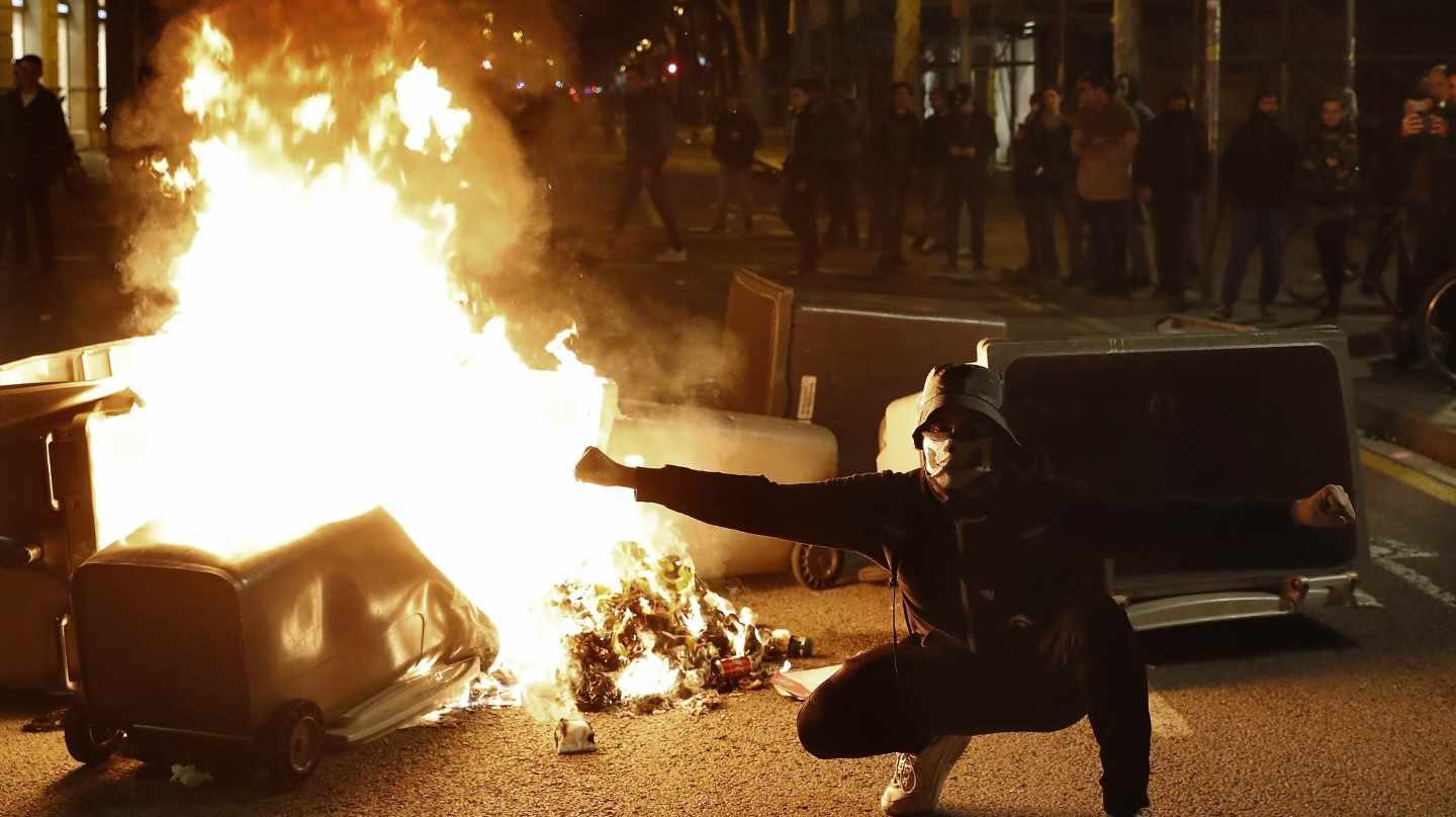 Un manifestante, junto a uno de los contenedores incendiados en Barcelona durante los disturbios del 25 de marzo.