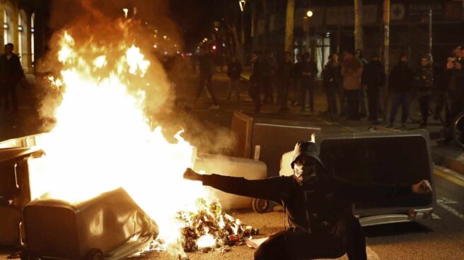 Un manifestante, junto a uno de los contenedores incendiados en Barcelona durante los disturbios del 25 de marzo.