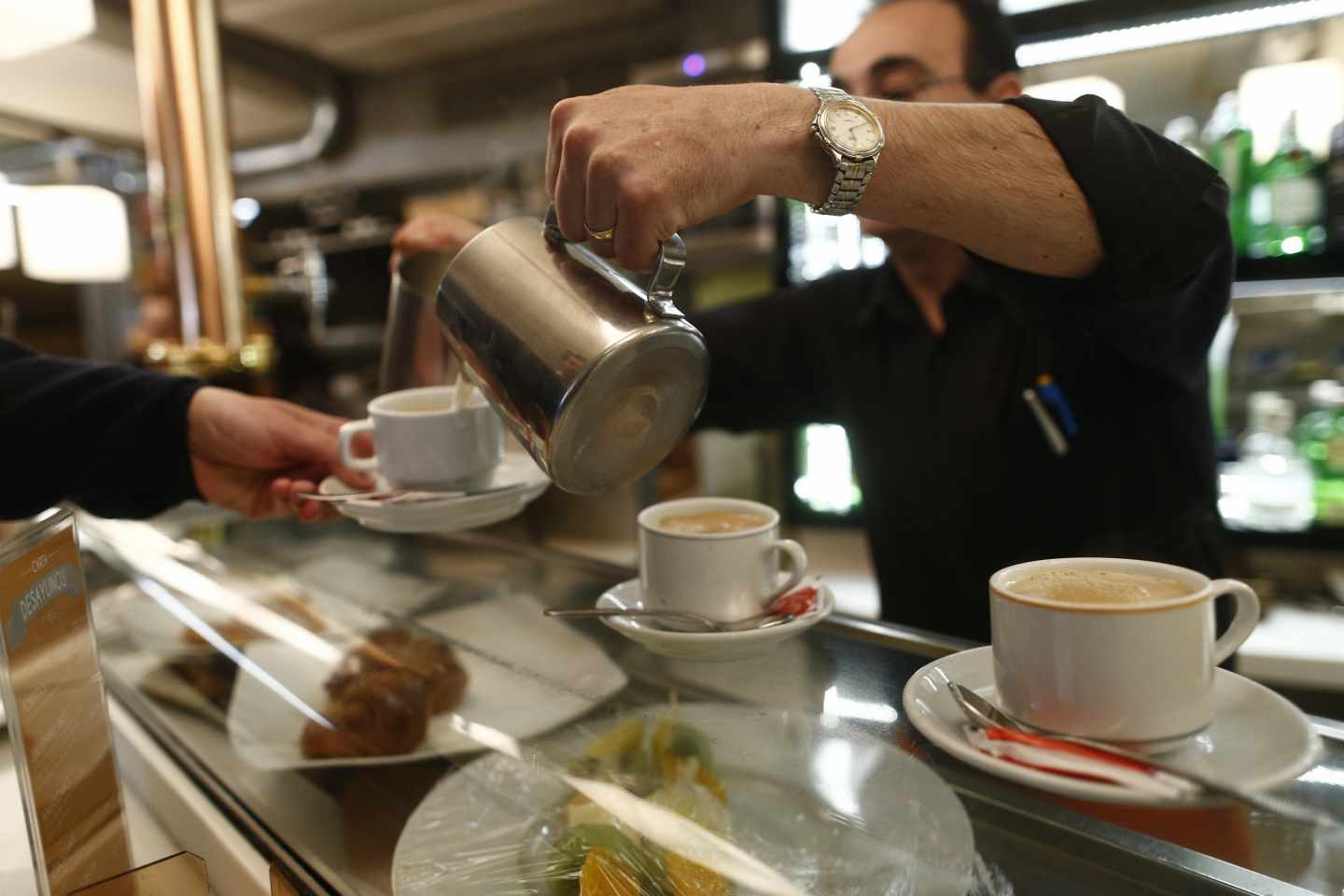 Un camarero sirve unos cafés dentro de un bar