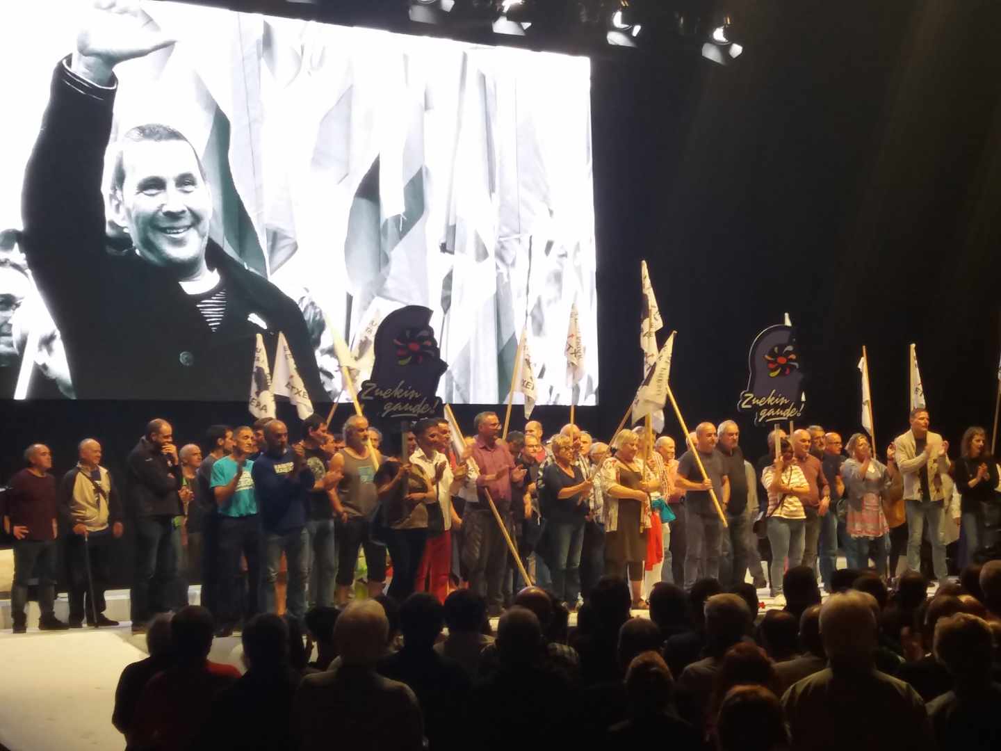 Presos de ETA son aplaudidos en el escenario del Bilbao Arena durante el acto de Sortu sobre una imagen de Arnaldo Otegi.