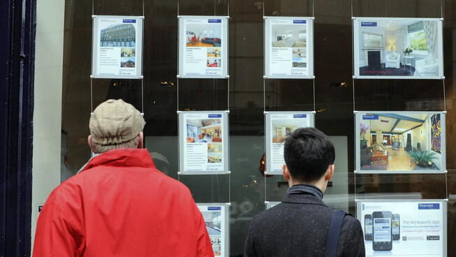 Alquiler Dos viandantes observan anuncios de alquiler y venta de casas en una inmobiliaria.