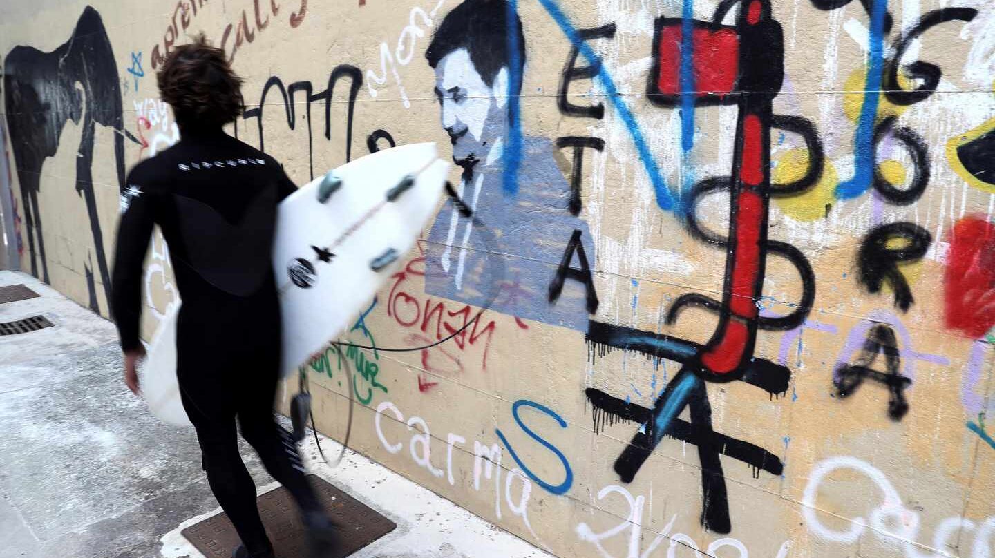 Un surfista pasa indiferente ante una pintada de ETA.