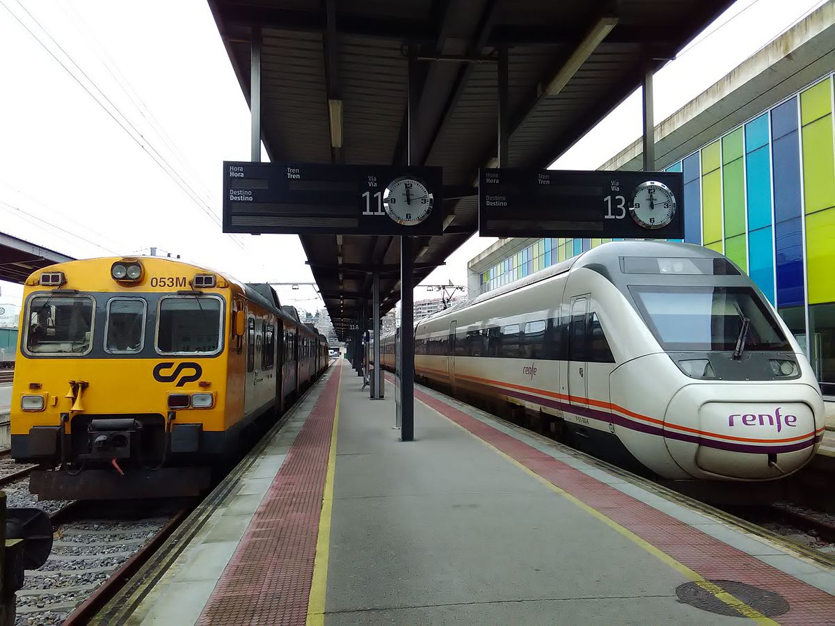 Un tren de CP (Portugal) y otro de Renfe parados en una estación, en andenes contiguos.