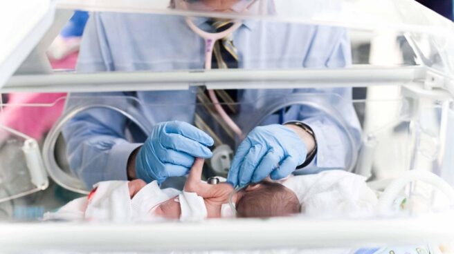 Imagen de un bebé en una incubadora siendo atendido por un sanitario