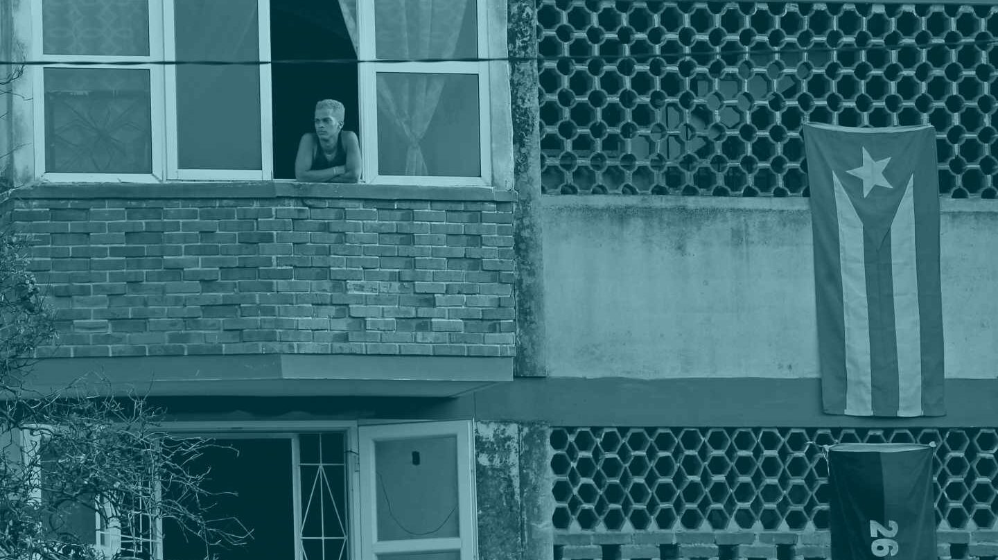 Una persona se asoma a la ventana en un edificio adornado con la bandera cubana.