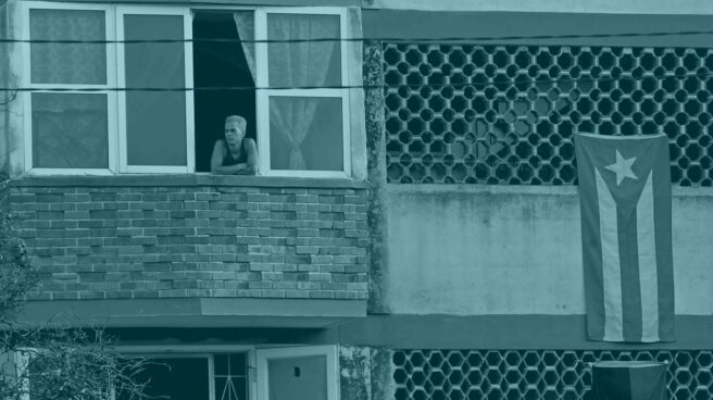 Una persona se asoma a la ventana en un edificio adornado con la bandera cubana.