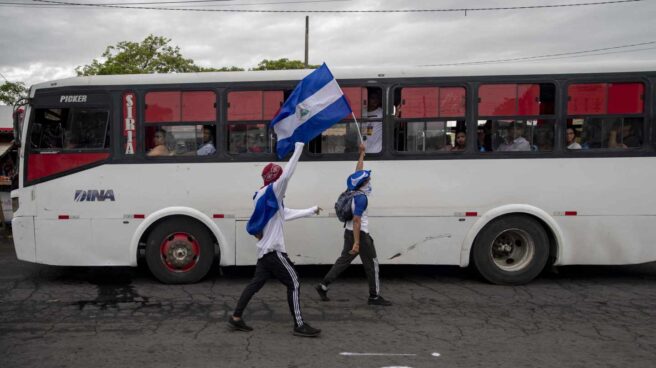 Dos jóvenes con las caras tapadas y una bandera de Nicaragua caminan frente a un vehículo de transporte público durante una protesta por 6 por el ciento del presupuesto nacional a las universidades, y la autonomía en las mismas hoy, jueves 2 de agosto de 2018, en el día numero 107 de protestas contra el gobierno de Daniel Ortega, frente a la Universidad Centroamericana (UCA), en Managua (Nicaragua). Los alumnos de la UCA, quienes habían organizado un plantón para este jueves para reclamar los fondos de ley que el Gobierno había negado al centro de estudios superiores, siguieron adelante con la protesta, pese a que la pasada noche, el Ejecutivo informó de que en el mes de agosto realizará el desembolso correspondiente.