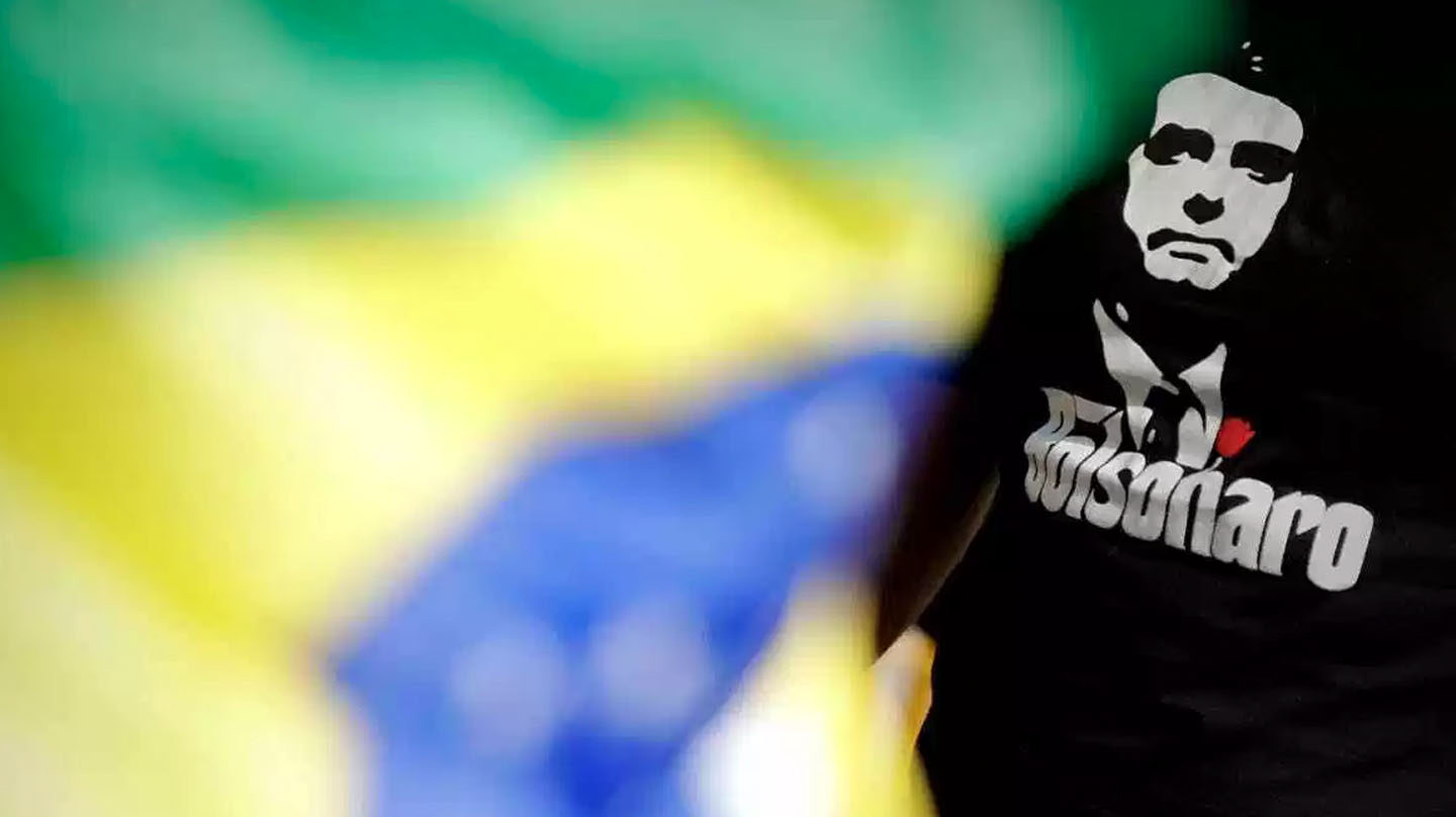 Un seguidor de Bolsonaro muestra el rostro de su ídolo en la camiseta con los colores de la bandera de fondo.