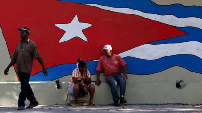 Dos cubanos se toman un respiro ante una bandera gigante en La Habana.
