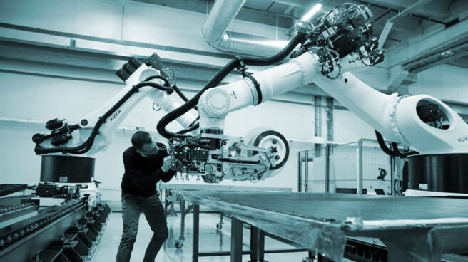 Un trabajador utiliza robots educados con Inteligencia Artificial en una cadena de montaje.