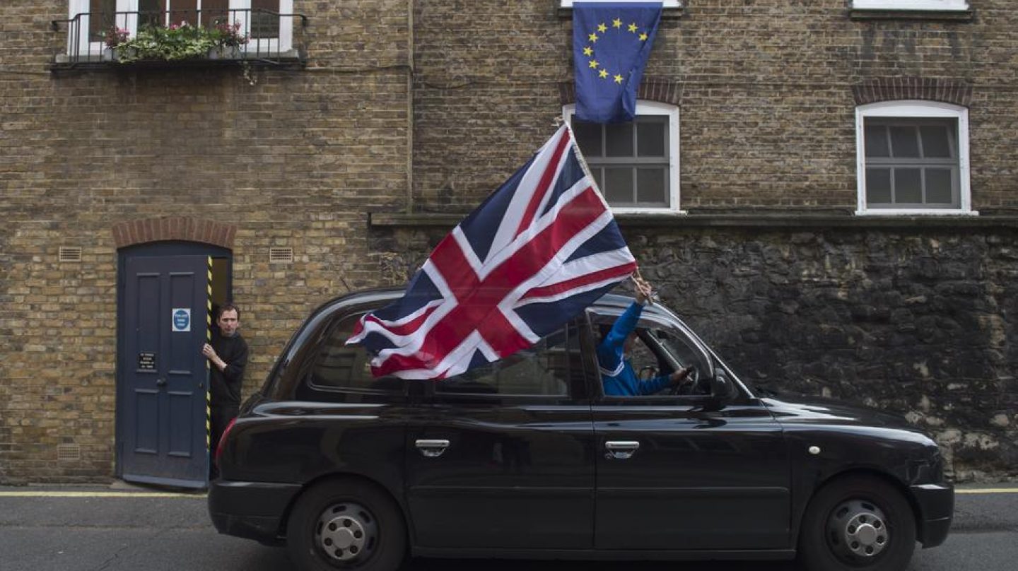 Un taxi con una bandera del Reino Unido pasa delante de una ventana con una bandera de la UE.