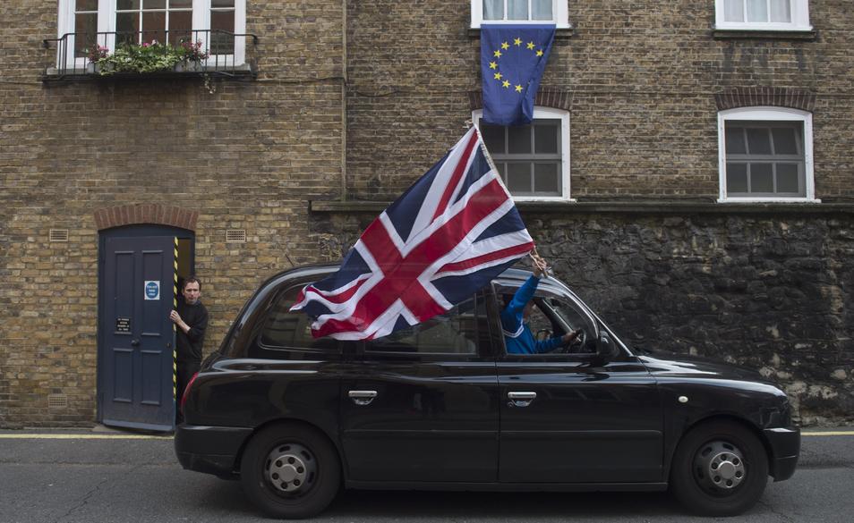 Un taxi con una bandera del Reino Unido pasa delante de una ventana con una bandera de la UE.