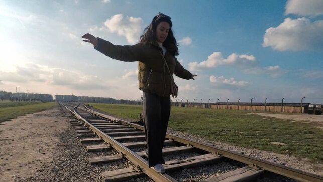 Una turista del campo de concentración de Auschwitz haciendo equilibrio sobre las vías férreas