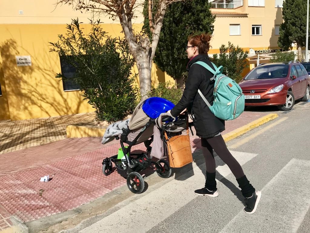 Una mujer cruza un paso de peatones con un carrito de bebé.