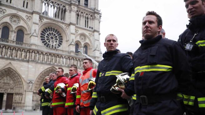 Un grupo de bomberos esperan la llegada del ministro del Interior ante Notre-Dame.