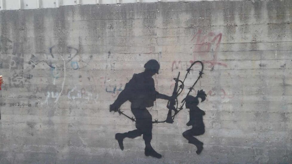 Un joven soldado israelí que no quiere servir en el Ejército sostiene la cuerda de espino ante una niña. El grafitero representa la decisión del soldado israelí de herir o no a la pequeña.
