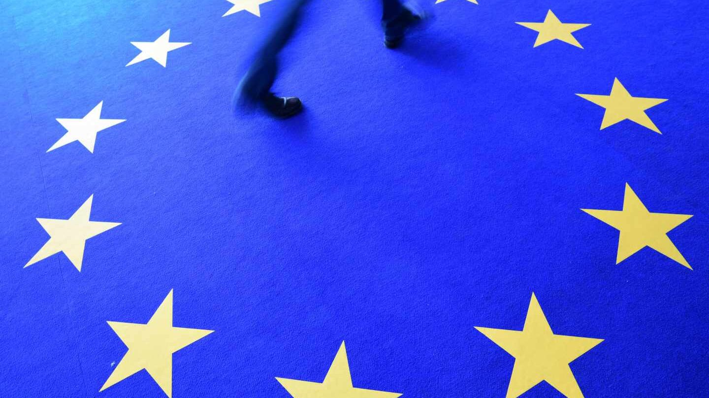 Un hombre pasa por un alfombra con las estrellas de la bandera de la UE.