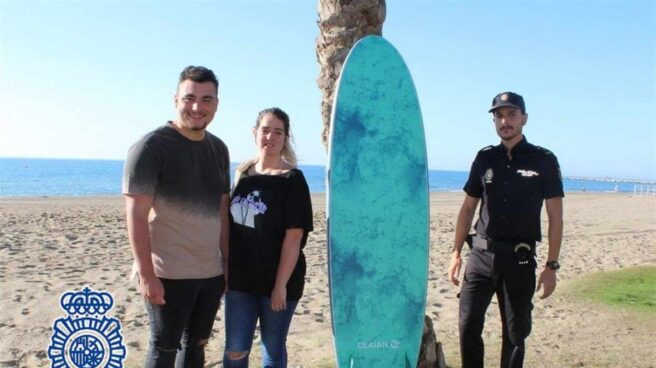 Agente con la tabla de surf y junto a los bañistas.