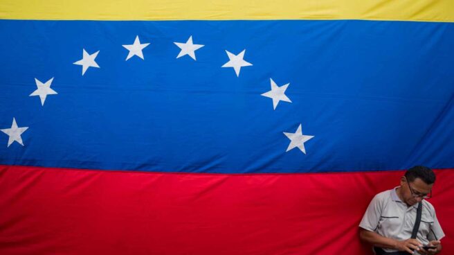 Bandera Venezuela Un venezolano revisa su móvil junto a una gran bandera de la República Bolivariana, en Caracas.
