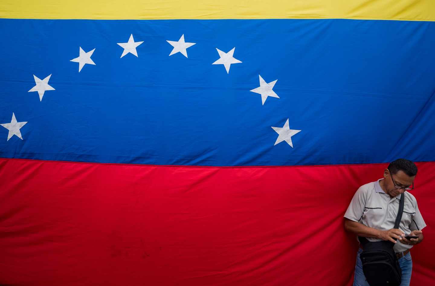 Un venezolano revisa su móvil junto a una gran bandera de la República Bolivariana, en Caracas.