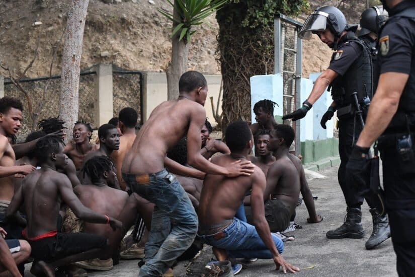 Uno de los de 153 migrantes, levanta los brazo a su entrada en Ceuta saltando su doble valla en lo que ha sido la primera incursión en grupo en un año.