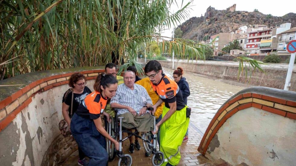 Voluntarios de protección civil trasladan a un hombre en silla de ruedas tras las intensas lluvias esta tarde en el barrio de Runes, Blanca, (Murcia)
